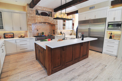 Large mountain style l-shaped light wood floor enclosed kitchen photo in Los Angeles with stainless steel appliances, a double-bowl sink, raised-panel cabinets, white cabinets, marble countertops, beige backsplash, stone tile backsplash and an island