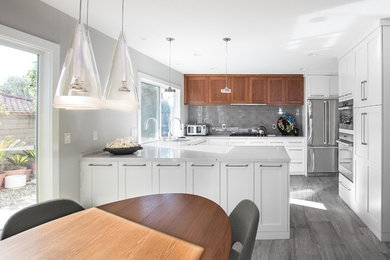 Photo of an expansive retro u-shaped open plan kitchen in Orange County with a single-bowl sink, shaker cabinets, white cabinets, composite countertops, grey splashback, ceramic splashback, stainless steel appliances, porcelain flooring and a breakfast bar.