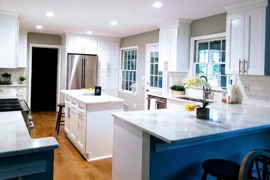Example of a large transitional u-shaped medium tone wood floor and brown floor enclosed kitchen design in Miami with shaker cabinets, white cabinets, quartz countertops, white backsplash, subway tile backsplash, stainless steel appliances, an island, white countertops and an undermount sink