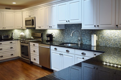 Mid-sized transitional galley dark wood floor enclosed kitchen photo in New York with an undermount sink, white cabinets, granite countertops, multicolored backsplash, stainless steel appliances and no island