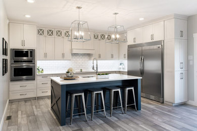 Inspiration for a medium sized classic u-shaped kitchen/diner in Toronto with a double-bowl sink, recessed-panel cabinets, grey cabinets, engineered stone countertops, white splashback, metro tiled splashback, stainless steel appliances, porcelain flooring, an island, grey floors and white worktops.