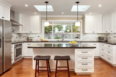 Large transitional u-shaped medium tone wood floor and brown floor eat-in kitchen photo in San Francisco with shaker cabinets, white cabinets, granite countertops, multicolored backsplash, stainless steel appliances, an island, black countertops, an undermount sink and marble backsplash