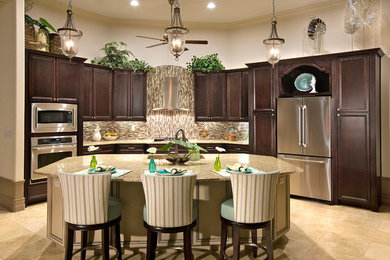 Open concept kitchen - large tropical l-shaped travertine floor and beige floor open concept kitchen idea in Tampa with a drop-in sink, recessed-panel cabinets, dark wood cabinets, granite countertops, stainless steel appliances, an island, multicolored backsplash, glass tile backsplash and brown countertops