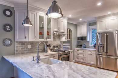 Inspiration for a mid-sized transitional u-shaped medium tone wood floor and brown floor eat-in kitchen remodel in Bridgeport with a farmhouse sink, recessed-panel cabinets, white cabinets, marble countertops, gray backsplash, stainless steel appliances, a peninsula and subway tile backsplash