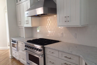 Inspiration for a large transitional light wood floor kitchen remodel in Philadelphia with shaker cabinets, white cabinets, marble countertops, white backsplash, subway tile backsplash, stainless steel appliances and an island