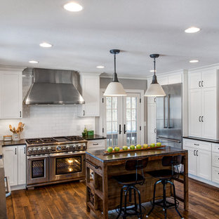 Foto di una cucina a L country con lavello stile country, ante in stile shaker, ante bianche, paraspruzzi bianco, paraspruzzi con piastrelle diamantate, elettrodomestici in acciaio inossidabile, parquet scuro, isola e top nero