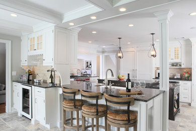 Eat-in kitchen - large transitional u-shaped travertine floor eat-in kitchen idea in New York with recessed-panel cabinets, a farmhouse sink, granite countertops, white cabinets, beige backsplash, stone tile backsplash, paneled appliances and an island