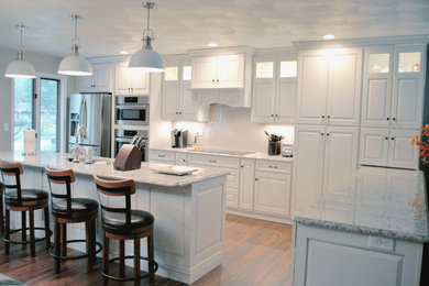 Inspiration for a transitional l-shaped medium tone wood floor open concept kitchen remodel in St Louis with raised-panel cabinets, white cabinets, granite countertops, white backsplash, ceramic backsplash, stainless steel appliances and an island