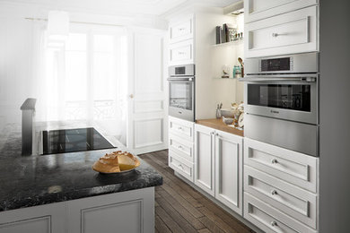 Ejemplo de cocina comedor clásica renovada con electrodomésticos de acero inoxidable, puertas de armario blancas, salpicadero blanco, una isla y suelo marrón