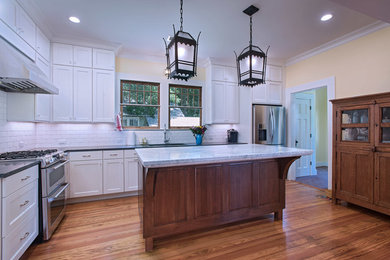 Example of a mid-sized transitional l-shaped medium tone wood floor and brown floor enclosed kitchen design in Austin with an undermount sink, shaker cabinets, white cabinets, granite countertops, white backsplash, subway tile backsplash, stainless steel appliances, an island and black countertops