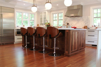 Example of a mid-sized transitional u-shaped dark wood floor eat-in kitchen design in Boston with a farmhouse sink, shaker cabinets, white cabinets, quartz countertops, gray backsplash, stone slab backsplash, stainless steel appliances and an island