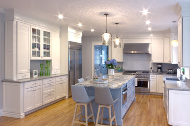 Inredning av ett klassiskt stort kök, med en undermonterad diskho, skåp i shakerstil, vita skåp, bänkskiva i kvarts, rostfria vitvaror, ljust trägolv, en köksö och brunt golv
