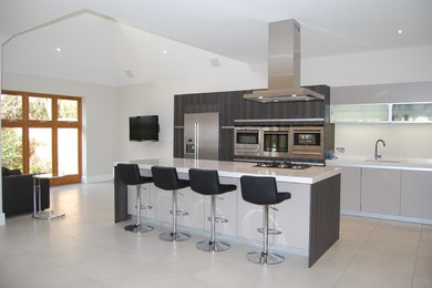 Large contemporary single-wall open plan kitchen in London with a submerged sink, flat-panel cabinets, grey cabinets, composite countertops, integrated appliances, ceramic flooring and an island.