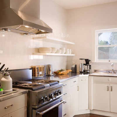 Kitchen - traditional l-shaped kitchen idea in Austin with stainless steel appliances, stainless steel countertops, a drop-in sink, flat-panel cabinets, white cabinets and white backsplash