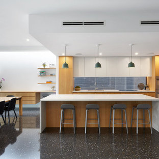 This is an example of a contemporary l-shaped open plan kitchen in Melbourne with a double-bowl sink, flat-panel cabinets, medium wood cabinets, window splashback, stainless steel appliances, with island, black floor and white benchtop.