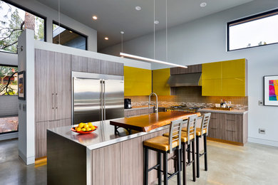 Example of a mid-sized trendy l-shaped concrete floor open concept kitchen design in Other with flat-panel cabinets, medium tone wood cabinets, stainless steel countertops, beige backsplash, matchstick tile backsplash, stainless steel appliances and an island