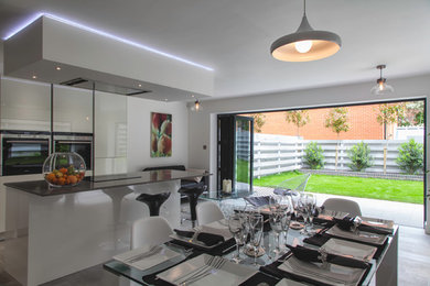 This is an example of a contemporary kitchen/diner in West Midlands with glass-front cabinets, white cabinets, quartz worktops, grey splashback, stainless steel appliances and an island.