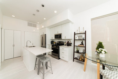 Mid-sized danish l-shaped laminate floor and gray floor kitchen pantry photo in Cleveland with an undermount sink, flat-panel cabinets, white cabinets, marble countertops, white backsplash, subway tile backsplash, stainless steel appliances and an island