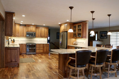 Example of a classic medium tone wood floor and brown floor kitchen design in Other with an undermount sink, medium tone wood cabinets, beige backsplash, mosaic tile backsplash, stainless steel appliances and an island