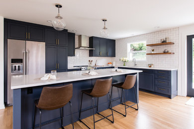 Eat-in kitchen - mid-sized transitional l-shaped dark wood floor and brown floor eat-in kitchen idea in Seattle with a drop-in sink, shaker cabinets, blue cabinets, quartz countertops, white backsplash, ceramic backsplash, stainless steel appliances, an island and white countertops