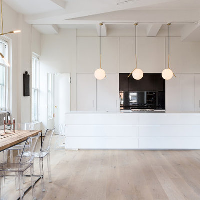 Eat-in kitchen - mid-sized scandinavian galley light wood floor eat-in kitchen idea in New York with flat-panel cabinets, white cabinets, an island, solid surface countertops, black backsplash, stainless steel appliances and glass sheet backsplash