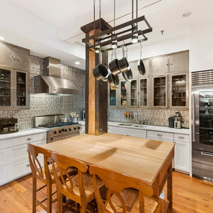 Photo of a transitional l-shaped kitchen in New York with a double-bowl sink, glass-front cabinets, stainless steel cabinets, metallic splashback, metal splashback, stainless steel appliances, medium hardwood floors and with island.