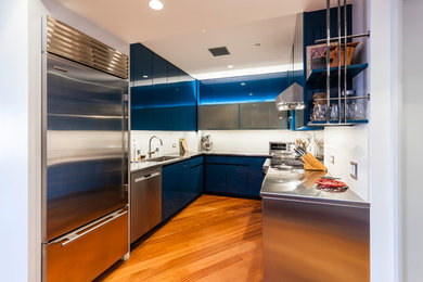 ニューヨークにあるコンテンポラリースタイルのおしゃれなコの字型キッチン (アンダーカウンターシンク、フラットパネル扉のキャビネット、青いキャビネット、ステンレスカウンター、白いキッチンパネル、石スラブのキッチンパネル、シルバーの調理設備、淡色無垢フローリング) の写真