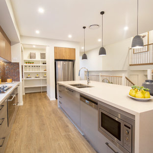 This is an example of a contemporary u-shaped kitchen in Sydney with a double-bowl sink, flat-panel cabinets, grey cabinets, red splashback, stainless steel appliances, medium hardwood floors, with island, brown floor and white benchtop.