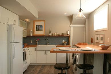 Small minimalist l-shaped eat-in kitchen photo in Vancouver with a farmhouse sink, glass-front cabinets, white cabinets, wood countertops, blue backsplash, ceramic backsplash, white appliances and a peninsula