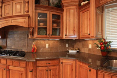 Elegant kitchen photo in Boise with a double-bowl sink, raised-panel cabinets, medium tone wood cabinets, granite countertops and stone tile backsplash