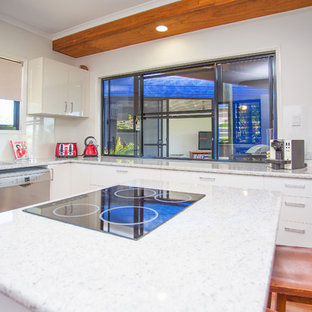 Design ideas for a mid-sized tropical l-shaped open plan kitchen in Other with laminate benchtops, white splashback, glass sheet splashback, with island, dark hardwood floors, a double-bowl sink, flat-panel cabinets, white cabinets, stainless steel appliances, white benchtop and wood.
