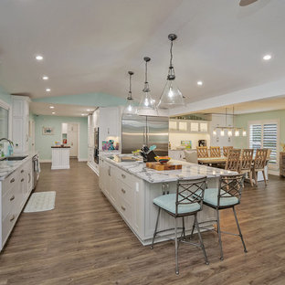 Photo of a large tropical open plan kitchen in Jacksonville with shaker cabinets, white cabinets, quartz benchtops, white splashback, ceramic splashback, stainless steel appliances, vinyl floors, multiple islands and grey benchtop.