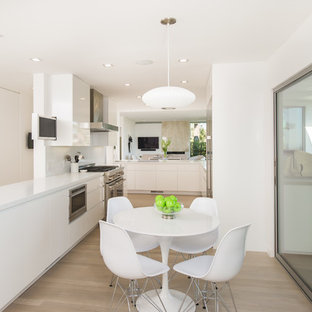 Open concept kitchen - contemporary galley light wood floor and beige floor open concept kitchen idea in Los Angeles with flat-panel cabinets, white cabinets and stainless steel appliances