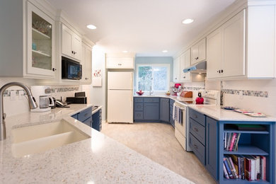 Klassisk inredning av ett mellanstort kök, med en undermonterad diskho, skåp i shakerstil, blå skåp, bänkskiva i glas, flerfärgad stänkskydd, stänkskydd i keramik, vita vitvaror, linoleumgolv, en halv köksö och beiget golv