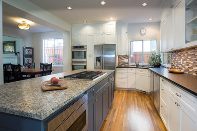 Inspiration for a mid-sized timeless l-shaped medium tone wood floor eat-in kitchen remodel in Portland with an undermount sink, white cabinets, granite countertops, brown backsplash, mosaic tile backsplash, stainless steel appliances and an island