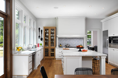 Large transitional l-shaped medium tone wood floor and brown floor eat-in kitchen photo in Vancouver with a single-bowl sink, shaker cabinets, white cabinets, marble countertops, gray backsplash, ceramic backsplash, stainless steel appliances, an island and white countertops