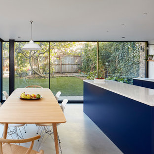Inspiration for a large contemporary galley open plan kitchen in London with flat-panel cabinets, blue cabinets, concrete flooring, an island, grey floors, white splashback, a built-in sink, quartz worktops, ceramic splashback, stainless steel appliances and white worktops.