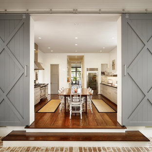 Imagen de cocina comedor de galera, campestre, grande, con armarios estilo shaker, electrodomésticos de acero inoxidable, suelo de madera en tonos medios, puertas de armario beige y una isla