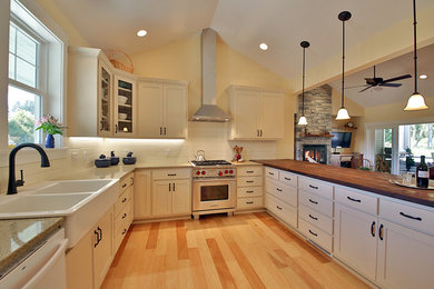 Large country u-shaped light wood floor eat-in kitchen photo in Seattle with a farmhouse sink, recessed-panel cabinets, white cabinets, wood countertops, white backsplash, subway tile backsplash, stainless steel appliances and a peninsula