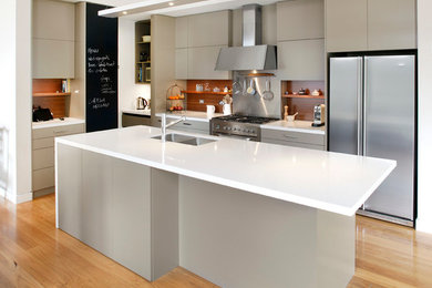 Photo of a medium sized contemporary l-shaped kitchen/diner in Sydney with a submerged sink, flat-panel cabinets, engineered stone countertops, brown splashback, beige cabinets, wood splashback, stainless steel appliances, light hardwood flooring and an island.