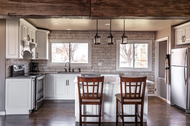 Foto på ett mellanstort rustikt grå kök, med en undermonterad diskho, luckor med upphöjd panel, vita skåp, bänkskiva i kvartsit, vitt stänkskydd, stänkskydd i tegel, rostfria vitvaror, laminatgolv, en köksö och brunt golv