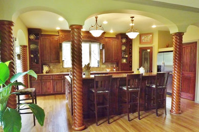 Example of a tuscan medium tone wood floor kitchen design in Seattle with an undermount sink, raised-panel cabinets, dark wood cabinets, granite countertops, beige backsplash and an island