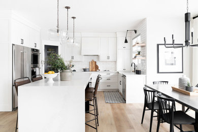 Inspiration for a scandinavian l-shaped kitchen/diner in Calgary with a belfast sink, shaker cabinets, white cabinets, engineered stone countertops, white splashback, porcelain splashback, stainless steel appliances, an island, beige floors and white worktops.