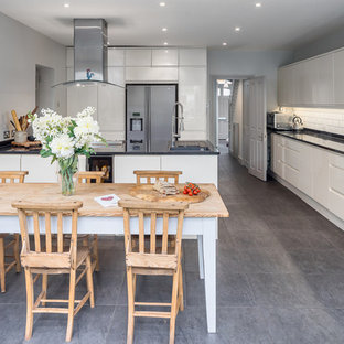 This is an example of a medium sized contemporary single-wall kitchen/diner in London with a submerged sink, flat-panel cabinets, white cabinets, white splashback, metro tiled splashback, grey floors and black worktops.