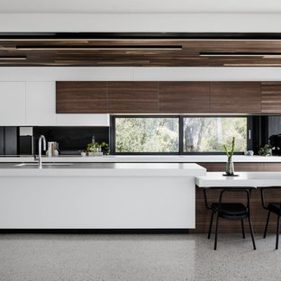 This is an example of a contemporary galley open plan kitchen in Melbourne with an undermount sink, flat-panel cabinets, dark wood cabinets, black splashback, window splashback, coloured appliances, with island, grey floor and white benchtop.