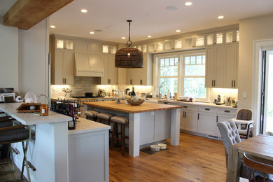 Large farmhouse u-shaped kitchen/diner in San Francisco with a belfast sink, beaded cabinets, white cabinets, granite worktops, white splashback, metro tiled splashback, stainless steel appliances, light hardwood flooring and multiple islands.