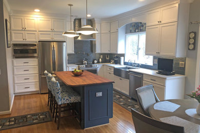 Inspiration for a large transitional l-shaped medium tone wood floor and brown floor eat-in kitchen remodel in DC Metro with a farmhouse sink, recessed-panel cabinets, white cabinets, quartz countertops, blue backsplash, glass tile backsplash, stainless steel appliances, an island and white countertops