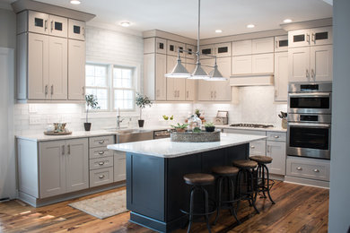 Kitchen pantry - large contemporary l-shaped medium tone wood floor and multicolored floor kitchen pantry idea in Raleigh with a farmhouse sink, white backsplash, stainless steel appliances, white countertops, shaker cabinets, white cabinets, marble countertops, an island and glass tile backsplash