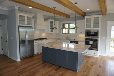 Open concept kitchen - large country l-shaped light wood floor and brown floor open concept kitchen idea in Birmingham with a farmhouse sink, raised-panel cabinets, white cabinets, granite countertops, white backsplash, porcelain backsplash, stainless steel appliances and an island