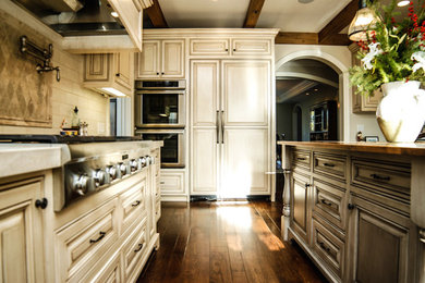 Inspiration for a mid-sized timeless l-shaped dark wood floor and brown floor kitchen remodel in San Francisco with raised-panel cabinets, granite countertops, beige backsplash, subway tile backsplash, paneled appliances, an island and distressed cabinets